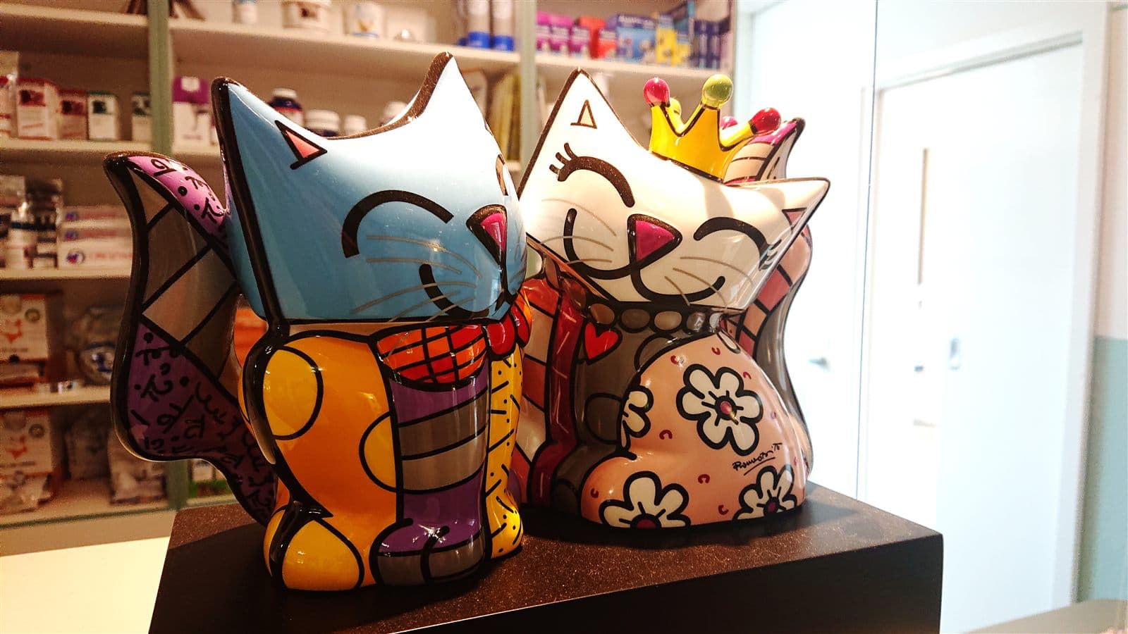 Bunte Katzenfiguren vor dem Regal der Praxisapotheke